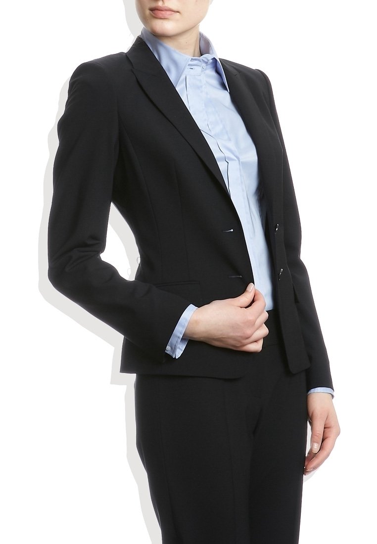 Blazer negro a medida con dos botones, solapas de muesca y bolsillos frontales, llevado sobre una camisa Dress de color azul claro con una textura suave.