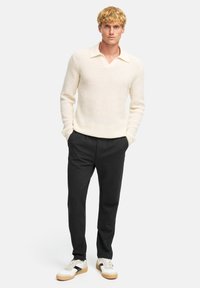 Maglione lavorato a maglia color crema con scollo a V e colletto a contrasto. Abbinato a pantaloni aderenti scuri e sneaker bianche con strisce nere.