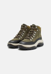 Zielone zamszowe buty hikingowe na czarnej gumowej podeszwie mają metalowe oczka, teksturowane sznurówki, wyściełaną podeszwę i wysoką konstrukcję dla wsparcia kostki.