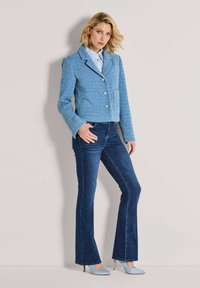 Blauw gestructureerd colbert met twee steekzakken aan de voorkant, zilverkleurige knopen, gecombineerd met donkerblauwe flared jeans en lichtblauwe, puntige hoge hakken.