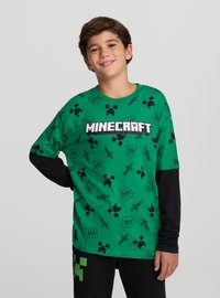 Maglietta verde a maniche lunghe con grafiche nere di Minecraft, tra cui volti di creeper, scatole di TNT e spade; scollo a girocollo.