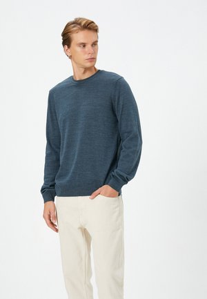 Crewneck sweater in donkerblauw breiwerk, met lange mouwen, geribbelde manchetten en zoom, gecombineerd met lichtbeige broek.