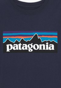 Námořnická látka s multibarevnou siluetou hor a výrazným bílým textem "patagonia" umístěným uprostřed oblasti hrudníku.