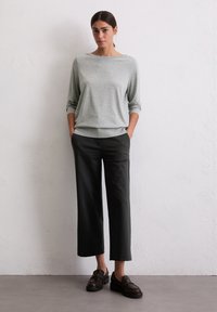 Helles graues Langarmshirt, lockere Passform, runder Ausschnitt, kombiniert mit dunklen, weit geschnittenen Hosen. Schwarze Loafer runden das Outfit ab.