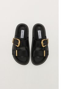 Black slide sandals made of smooth leather, featuring gold buckles and white stitching, with a flat sole and open toe design.