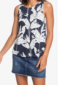 Granatowy bezrękawnik z białym nadrukiem botanicznym; miękka, lekka tkanina; w zestawie z dżinsową spódnicą mini z postrzępionym dołem.