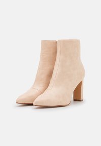 Bottes beige texturées jusqu'à la cheville, avec des bouts pointus et un talon bloc. Fabriquées en matériau synthétique avec des coutures simples le long des bords.