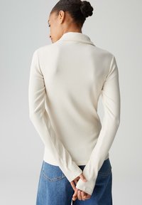 Maglione a maniche lunghe costellato, di colore bianco sporco, con collo piegato e polsini lunghi, abbinato a pantaloni in denim blu.
