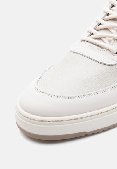 Κοντινή λήψη στο δάχτυλο λευκού δερμάτινου αθλητικού παπουτσιού με υφασμάτινο άνω μέρος, ραφές, κορδόνια και παχύ, εκρού καουτσούκ πέλμα σε φωτεινό φόντο.