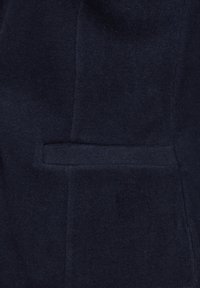 Tissu en laine marine au toucher lisse, doté d'une poche latérale et d'une coupe ajustée qui met en valeur un design structuré.