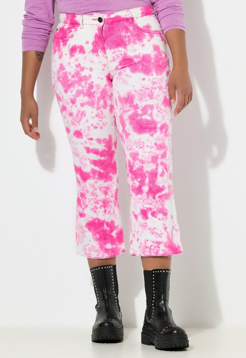Jeans recortados blancos con un patrón de tie-dye rosa, con cierre de botón y cremallera. Combinados con botas de tobillo negras con tachuelas.