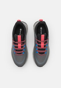 Scarpe da atletica grigie con bordature nere, dotate di una tomaia testurizzata, lacci rosa e blu, e un anello sul tallone per un facile indossamento.