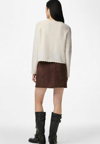 Kremowy, krótki sweter z falowanym dołem, zestawiony z brązową zamszową spódnicą. Długie czarne kozaki z klamrami widoczne od tyłu.