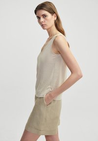 Top sin mangas de color beige con escote en V, hecho de una tela ligera. Combinado con pantalones cortos beige claros que cuentan con bolsillos laterales y dobladillo vuelto.