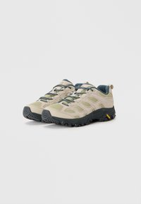 Pair of beige and green hiking shoes with black Vibram soles and blue patterned laces on a light background.