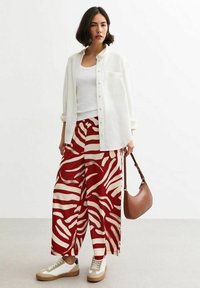 White button-up shirt, white tank top, red and cream striped wide-leg pants, beige sneakers, and a brown shoulder bag.