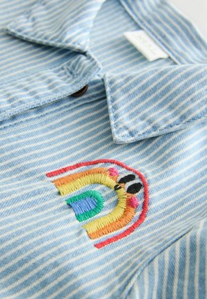 Jasnoniebieska kurtka dżinsowa w paski z kolorowym, haftowanym wzorem tęczy na piersi, z wykładanym kołnierzem i guzikami.