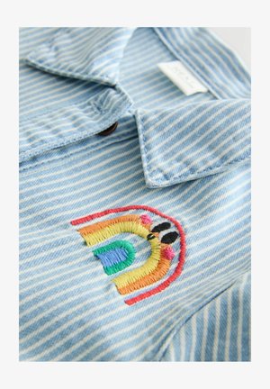 Vaaleansininen raidallinen farkkutakki, jossa monivärinen kirjailtu sateenkaari rinnassa, kärjellään varustettu kaulus ja napillinen yksityiskohta.