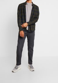 Camicia a quadri con bottoni in verde scuro e blu navy, t-shirt girocollo grigia, pantaloni grigi e sneakers grigie con dettagli testurizzati.