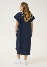 Rochie midi din bumbac bleumarin, cu mâneci scurte și crăpături laterale, având o croială lejeră și un tiv drept, asortată cu adidași albi.