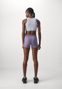 Vaaleanliila urheilu crop-top, jossa on teksturoidusta kankaasta valmistettu ja logobandi, yhdistettynä vastaaviin shortseihin. Tummat kengät harmaiden sukkien kanssa viimeistelevät asukokonaisuuden.