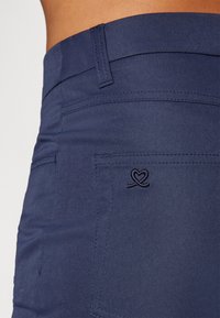 Navy blue pants made of smooth fabric, featuring a subtle heart-shaped embroidery on the back pocket and standard belt loops.