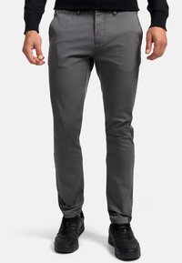 Pantalon gris à motifs, avec une coupe slim, fabriqué dans un tissu léger. Il dispose de poches latérales et est associé à des baskets noires.
