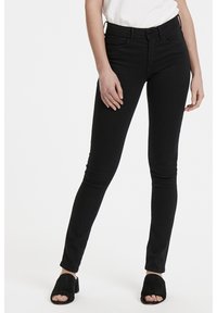 Černé skinny džíny vyrobené z denimu, s vysokým pasem, předními kapsami a hladkou strukturou, doplněné černými mules s otevřenou špičkou.