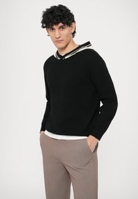 Fekete pulóver fehér és szürke csíkos gallérral, laza illeszkedéssel. Világosszürke nadrággal párosítva. Sima tapintású, kényelmes, hétköznapi stílus.