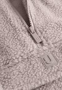 Polarowa kurtka zapinana na zamek w jasnoszarym kolorze z teksturowaną powierzchnią, z dopasowanym zamkiem i szczegółowym naszywką z logo.