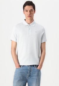 Ανοιχτό μπλε πόλο μπλουζάκι από μαλακό βαμβακερό ύφασμα, με τριπλό κουμπί, κοντά μανίκια και διακριτό λογότυπο κεντημένο στο στήθος.