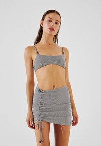 Bikini top s črnimi in belimi črtami z nastavljivimi naramnicami ter ujemajoča se mini krilca z bočnim vrvico in gumbom.
