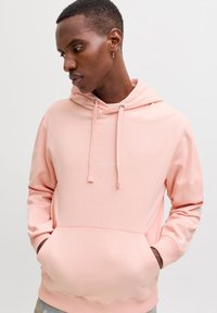 Felpa con cappuccio rosa chiaro con coulisse, tasca frontale e logo discreto sul petto. Realizzata in tessuto morbido e liscio con polsini a costine.