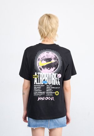 Camiseta de algodón negra con un gráfico circular que presenta un diseño de globo rosa, texto en negrita y nombres de ciudades. Logo de "Nike" en amarillo, "Just Do It" en rosa.