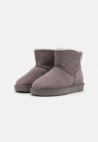 Bottines en suede gris avec une doublure intérieure confortable, bout arrondi et semelle en caoutchouc texturée. Détails de couture autour de la tige.