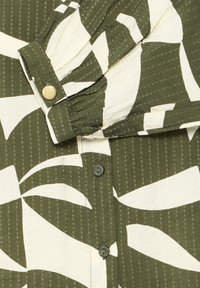 Grøn og hvid mønstret stof med lodrette striber, der har knapper og en manchet med en tekstureret guldknap.