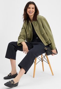 Olijfgroen cropped jack met een bruine kraag, marineblauwe wijde broek, zwarte loafers met gouden hardware en een kleine zwarte handtas.