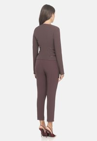 Giacca fitted color mogano con dettagli delle cuciture e pantaloni tapered coordinati. Tessuto liscio; indossata con sandali con taccoalto. Design minimalista.