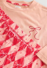 Short-sleeve peach shirt with ruffled red patterned skirt, featuring white bows and a diamond design. Soft fabric with a relaxed fit.