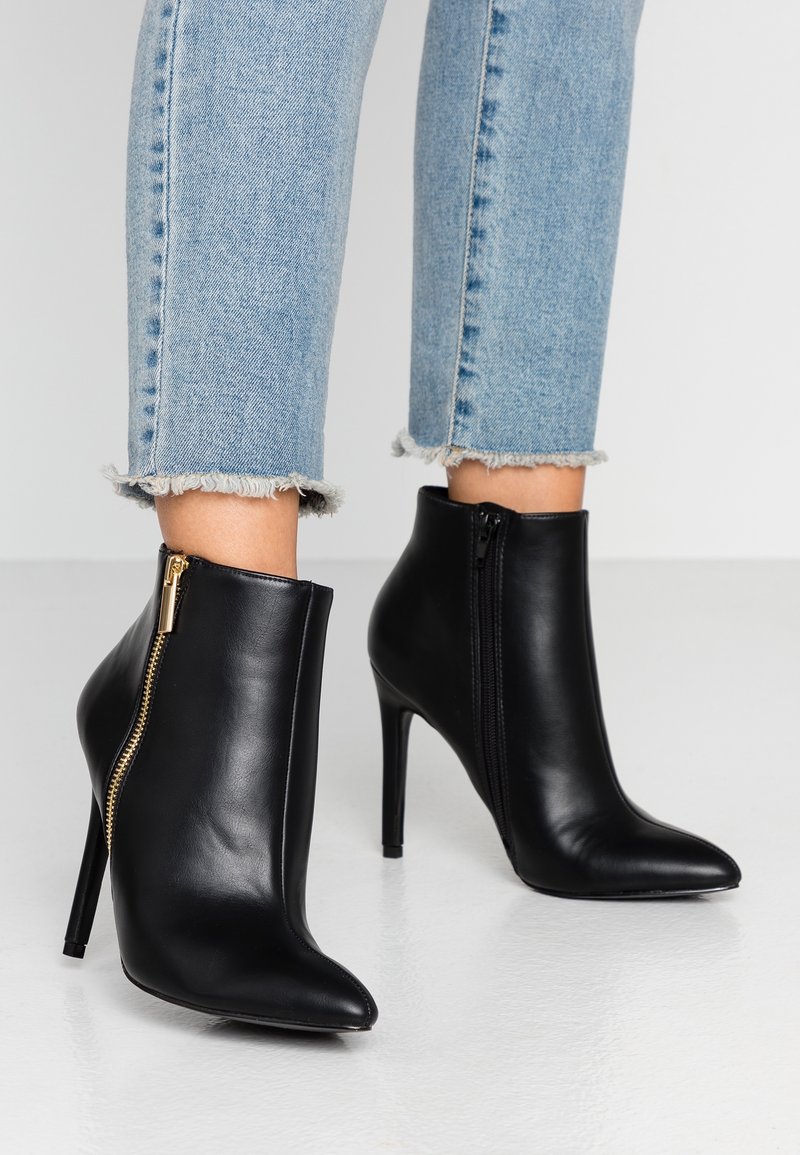 Bottes en cuir noir à bout pointu, talons aiguilles hauts et côtés zippés, portées avec un jean bleu clair à ourlet effiloché.