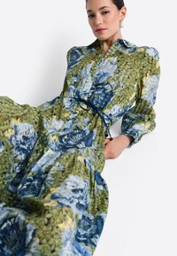 Kvetinové maxi šaty v zelenej, modrej a žltej farbe, s golierom, dlhými rukávmi a zúženým pásom s modrou šnúrkou. Textúrovaná látka s vrstvenými vzormi.