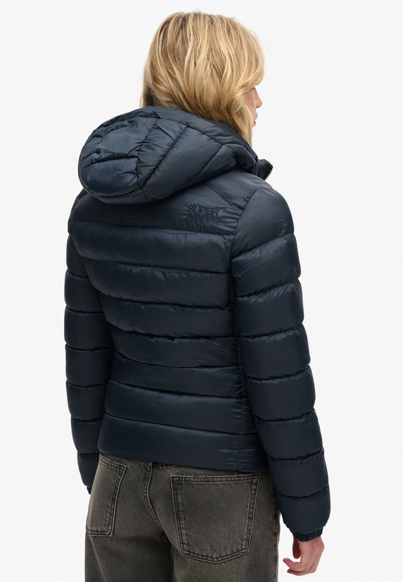 Marine pufferjack met capuchon, voorzien van horizontale stiknaden, ritssluiting en gegraveerd logo op de achterkant. Glad, glanzend oppervlak.