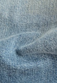Tela de mezclilla en azul claro con una textura suave y un sutil patrón de tejido diagonal, mostrando ligeras variaciones en el tono.