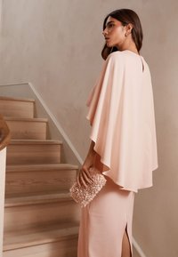 Jasnoróżowa sukienka z lejącym się kapturem, bocznym rozporkiem i teksturowaną torebką. Gładka tkanina i warstwowa konstrukcja tworzą miękką sylwetkę.