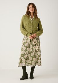 Green knitted cardigan with a textured pattern and clear buttons, layered over a floral patterned midi dress in shades of green and pink.