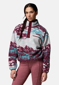 Sudadera de forro polar en azul, blanco y granate con patrones de montañas, cuello con media cremallera y bolsillo en el pecho. Tejido texturizado y acogedor con botones decorativos.
