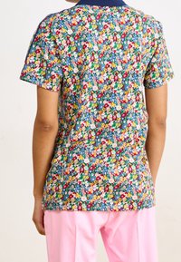 Kortärmad skjorta med ett blått blommönster i olika färger. Kragen är marinblå och den bärs med rosa byxor.