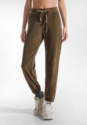 Pantalones jogger de terciopelo marrón con puños elásticos y cintura con cordón, usados con calcetines grises y zapatillas blancas gruesas.