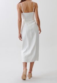 Bílé midi šaty s tenkými nastavitelnými ramínky, přiléhavým vrškem a bočním zipem. Hladká textura a jednoduchý, elegantní design.