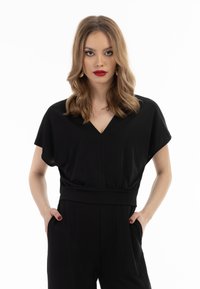 Schwarzer Jumpsuit mit kurzen, schwingenden Ärmeln, V-Ausschnitt und gerafftem Taillenbereich. Glattes Material mit lockerer Passform, ausgestattet mit seitlichen Taschen.